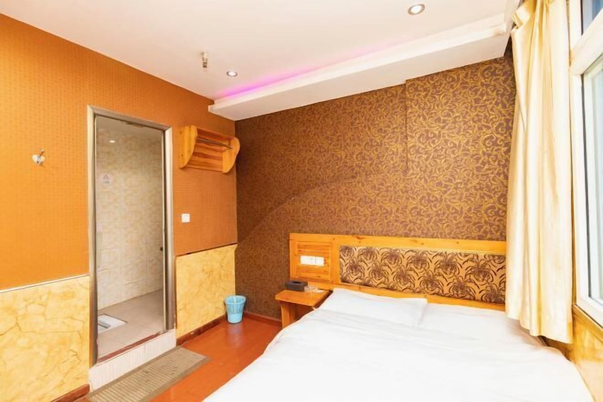 A hotel room with a bed, a wooden headboard, a shower area, and a window with curtains.