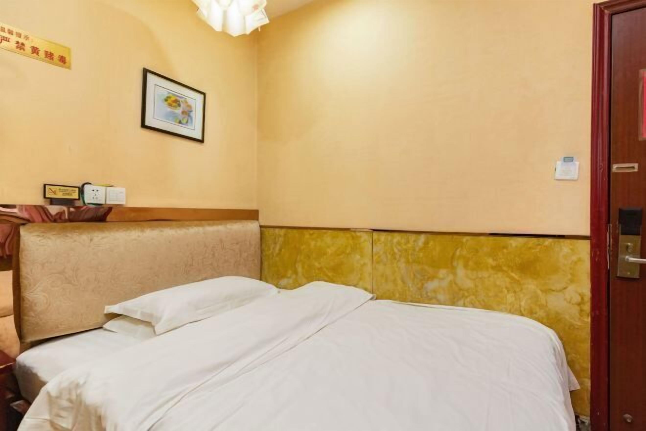 A hotel room with a bed, a headboard, a wall-mounted picture, and a door.