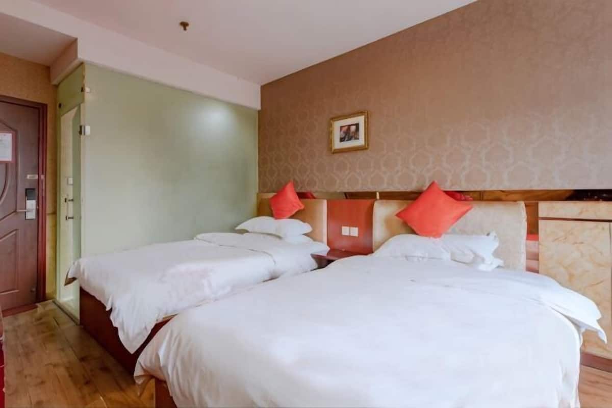 A hotel room with two beds, a wooden headboard, a door, and a wall with a framed picture.