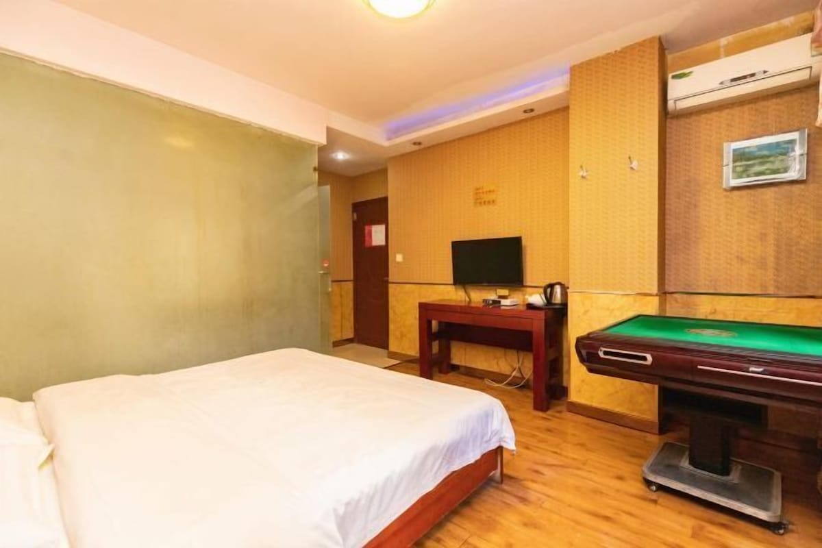 A hotel room with a bed, a desk, a television, and a pool table.