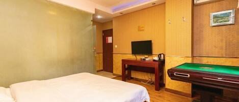 A hotel room with a bed, a desk, a television, and a pool table.