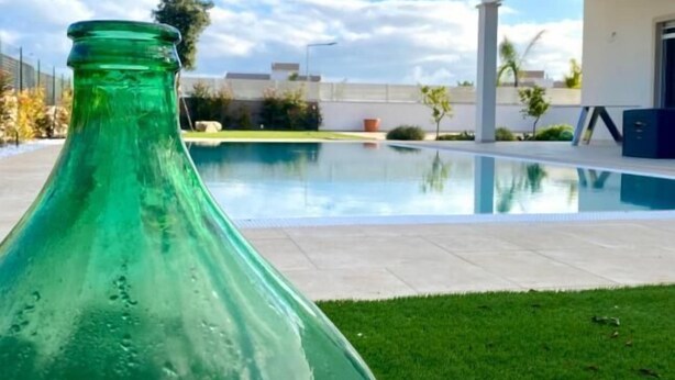 A green bottle in the foreground with a swimming pool and a modern house in the background. - Allegria Pool House (Monopoli)