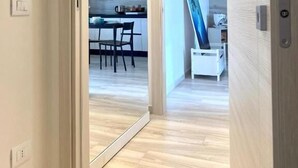 A modern interior with a wooden floor, a dining area with chairs and a table, and a kitchen with a counter and hanging lights. - Allegria Pool House (Monopoli)