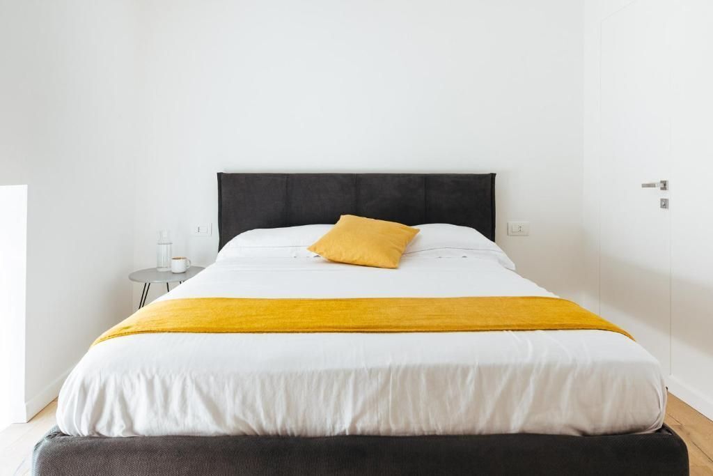 A neatly made bed with a black headboard, a yellow pillow, and a yellow throw blanket.