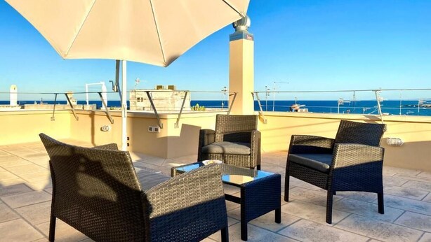 A terrace with wicker furniture and a large umbrella, overlooking a coastal view.