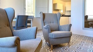 A living room with two armchairs, a dining table, and a kitchen area visible through an open door.