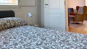 A bedroom with a bed, a window, a door, and a chair in the adjacent room.