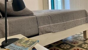 A bedroom with a bed, a bedside table with books, a lamp, and a wardrobe. - Rouge (Monopoli)
