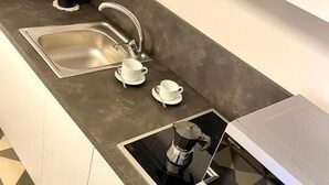 A modern kitchen with a stainless steel sink, two white cups, a coffee maker, and a microwave. - Rouge (Monopoli)