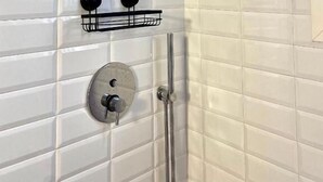 A shower area with white tiled walls, a handheld showerhead, a wall-mounted faucet, and a black towel rack. - Rouge (Monopoli)