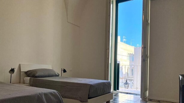 A room with two beds, a balcony with a view of buildings, and a tiled floor. - Rouge (Monopoli)