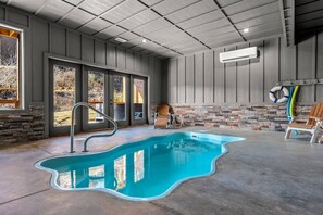 Ein moderner Innenpool mit klarem, blauem Wasser, einer Metallleiter und einer Wand aus Stein im Hintergrund.