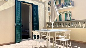 A small outdoor patio with a white table and chairs, a green door, and a balcony with a railing. - La Terrazzina (Monopoli)