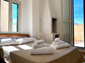 A hotel room with a bed, two windows, a lamp, and a view of the outside.