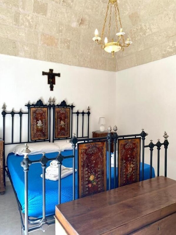 A bedroom with a bed, a cross on the wall, and a chandelier.