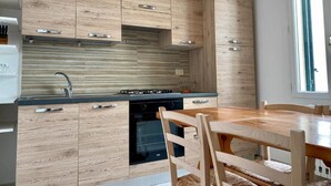 A modern kitchen with wooden cabinets, a built-in stove, and a dining area with a wooden table and chairs. - La Terrazzina (Monopoli)