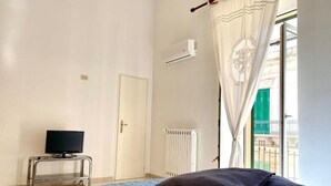 Een slaapkamer met een bed, een televisie op een standaard, een airconditioner en een raam met gordijnen.
