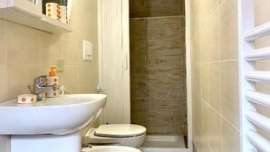 Een kleine badkamer met een wastafel, twee toiletten, een douche en een spiegel.