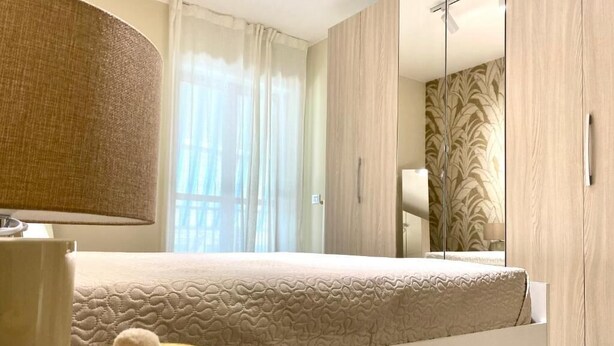 A modern bedroom with a bed, a bedside lamp, a small round table, and a mirror. - Bella Luna Apulian Living (Monopoli)