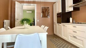 A modern kitchen with white cabinets, a dining table with chairs, a hanging light fixture, and a green wall with a plant. - Bella Luna Apulian Living (Monopoli)
