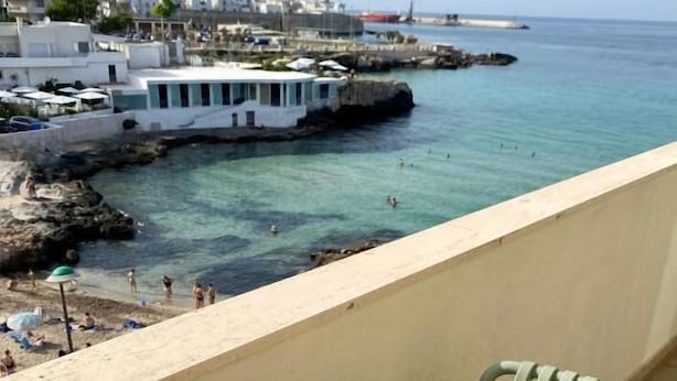 A balcony with a table and two mugs, overlooking a coastal area with buildings and a pier. - La Vue Est Belle (Monopoli)