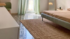 A modern bedroom with a bed, a desk, and a chair. There is a window with curtains, a radiator, and a ceiling light fixture. - La Vue Est Belle (Monopoli)