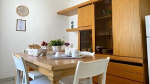 Un coin repas comprenant une table en bois, des chaises blanches, une horloge et des meubles en bois contenant de la verrerie.
