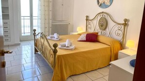 Une chambre à coucher comprenant un lit, des tables de chevet, un radiateur, une fenêtre avec des rideaux et un élément de décoration murale.