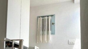 A laundry area with a washing machine, a small window with lace curtains, and a light switch on the wall. - Pearl of the Sea (Monopoli)