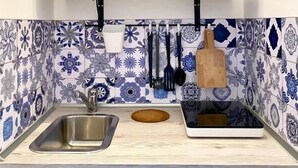 A kitchen with a sink, a wooden countertop, a backsplash with blue and white tiles, and a shelf above the countertop holding dishes and glasses. - Pearl of the Sea (Monopoli)