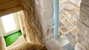 A stone-walled room with a small window, a door leading to another room, and a tiled floor. - Shell (Monopoli)