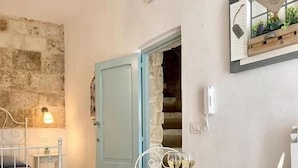 A room with a bed, a table with two chairs, a stone wall, and a door leading to another room. - Shell (Monopoli)
