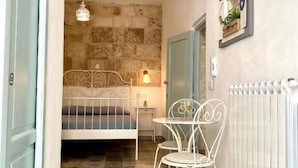 A narrow hallway with a bed, a table, and two chairs. - Shell (Monopoli)