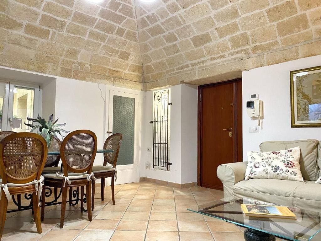 A living room with a dining area, a sofa, a glass coffee table, and a door with a security camera.