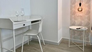 A modern, minimalist room with a white desk, a white chair, and a small table with a lamp. - Porto Bianco (Monopoli)