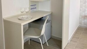 A compact, white room with a small desk and chair, a built-in shelving unit, and a compact kitchenette. - Red Port (Monopoli)