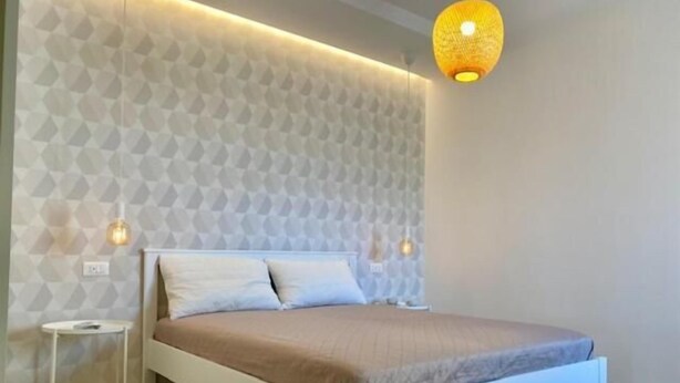 A modern bedroom with a geometric-patterned wall, a white bed, and two bedside lamps. - Red Port (Monopoli)
