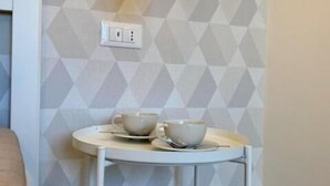 A room with a geometric-patterned wall, a white table with two cups and saucers, and a hanging light fixture. - Red Port (Monopoli)