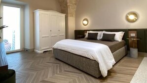 A bedroom with a herringbone-patterned floor, a bed with white and gray bedding, a white wardrobe, and a ceiling fan. - MARIACHIARA (Monopoli)