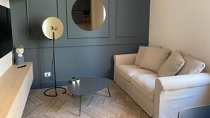 A modern living room with a grey accent wall, a round mirror, a beige sofa, and a small coffee table. - Matthias (Monopoli)