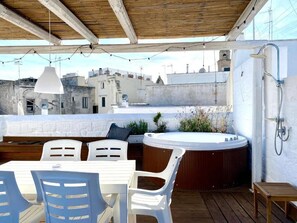 Een terras buiten met een houten tafel en stoelen, een jacuzzi en een douchegedeelte.