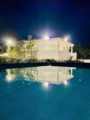 A modern building with a glass facade, a swimming pool in front, and a well-lit exterior at night. - Bella Luna Villa with Pool (Monopoli)