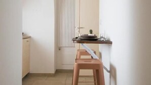 Un pasillo estrecho con un taburete de madera, un radiador y una pequeña mesa con platos.