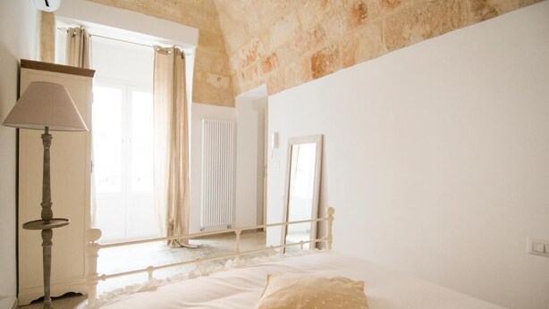 Un dormitorio con cama, lámpara, ventana con cortinas y techo de piedra.