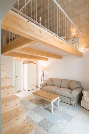 A spacious living area with a high ceiling, wooden beams, a sofa, a coffee table, and a staircase.