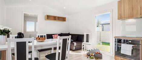 A modern kitchen with white cabinetry, a dining area with white chairs, and a view of the outdoors.