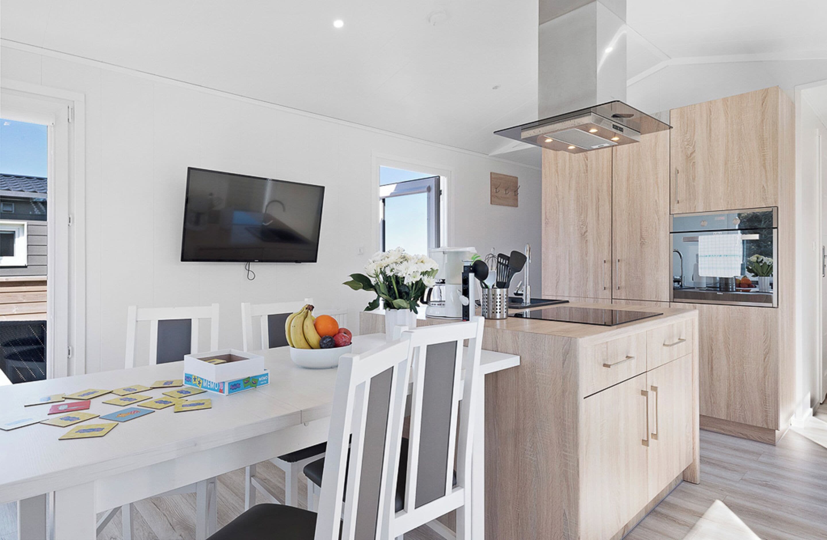 Een moderne keuken met witte kasten, een inbouwoven en een flatscreen televisie boven de aanrecht.