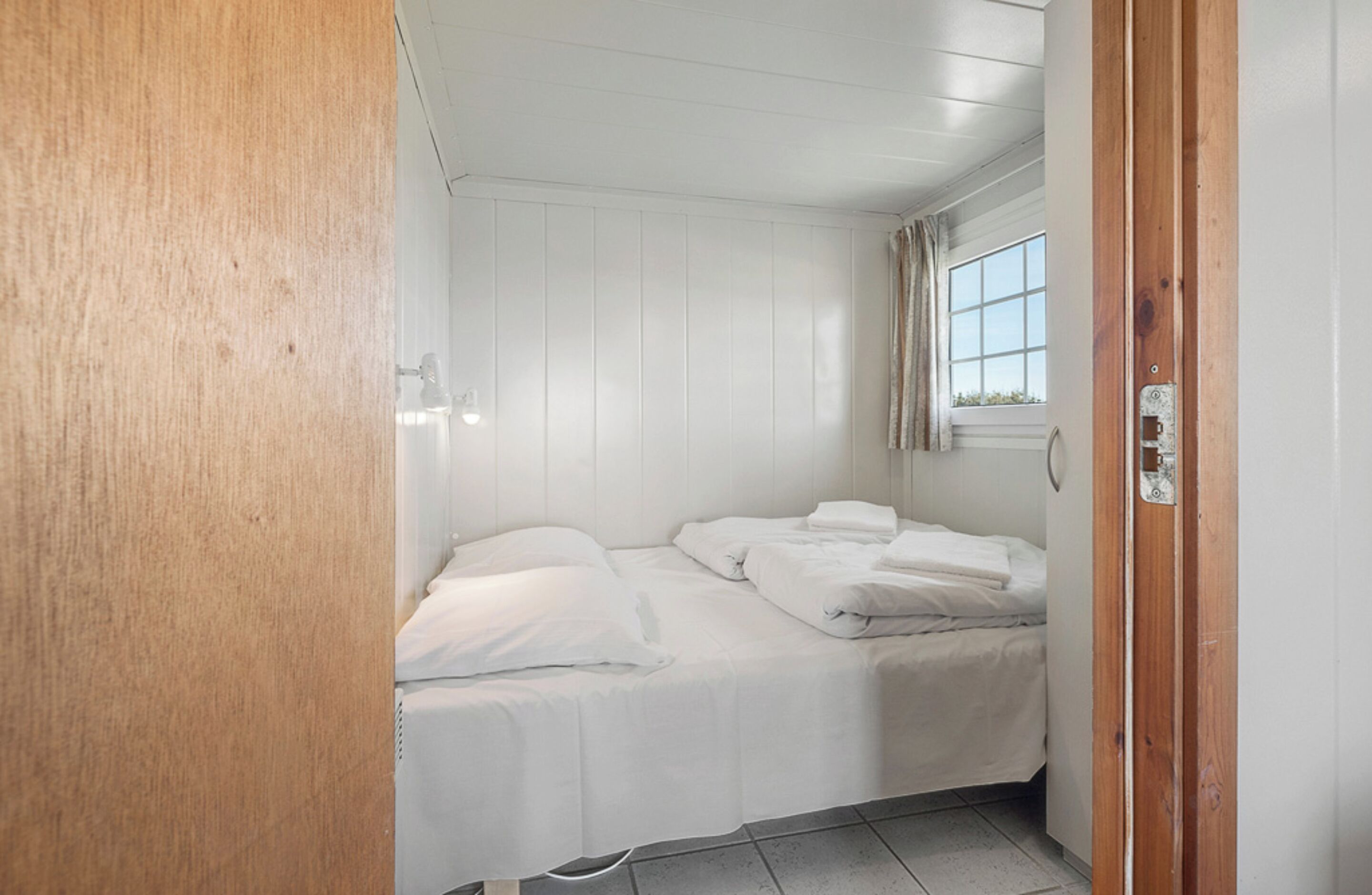 Ein kleines Zimmer mit einem Einzelbett, weißen Wänden und einer Holztür.