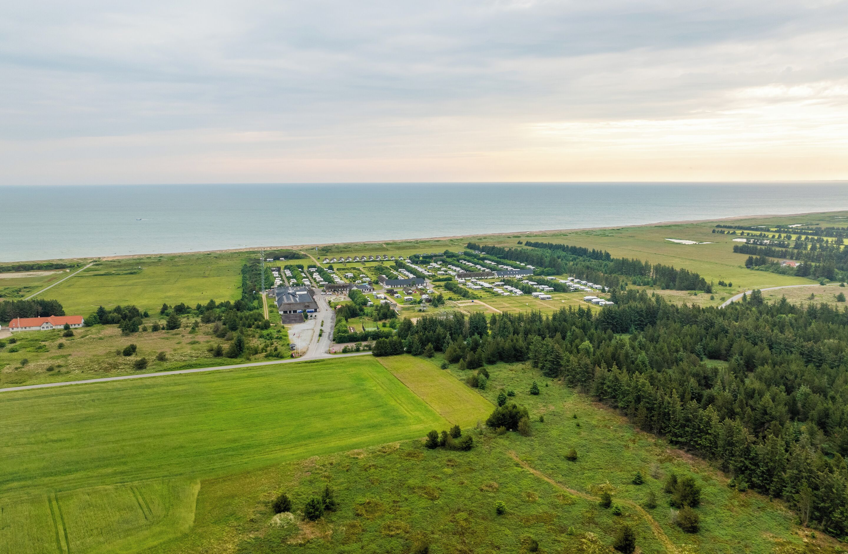 An aerial view of a coastal property with a main building, several smaller structures, and extensive green fields.