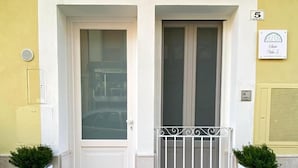 A building entrance with a white door and a balcony with a metal railing. There are two potted plants on either side of the door. - Vitti Suite 5 (Monopoli)